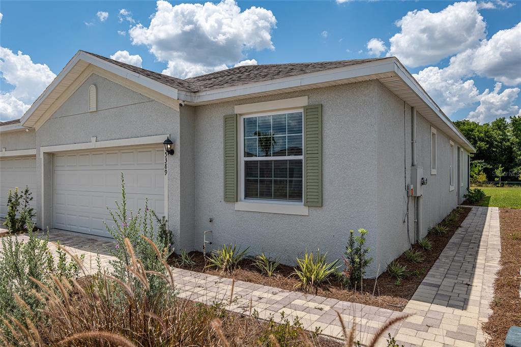 A single-story house exterior with a garage, a paved walkway, and green window shutters — 5389 NW 48TH PLACE, OCALA, FL