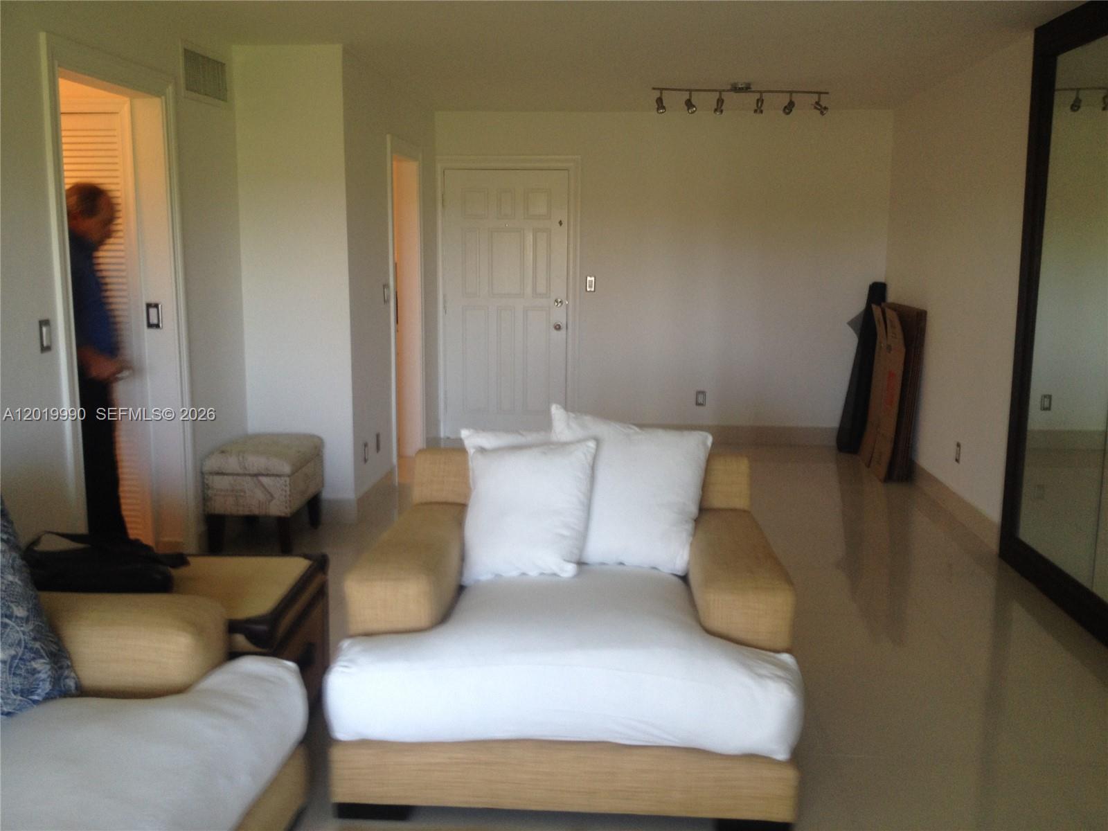 A living room features light-colored tile floors, a tan armchair, and a white door — 6855 Edgewater Dr, Coral Gables FL 33133, CORAL GABLES, FL
