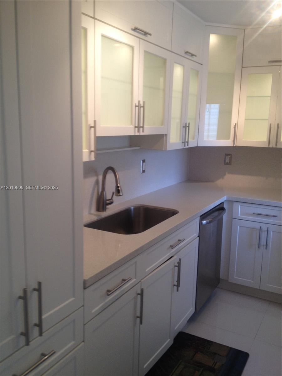A kitchen features white cabinets with glass inserts, stainless steel appliances, and light countertops — 6855 Edgewater Dr, Coral Gables FL 33133, CORAL GABLES, FL