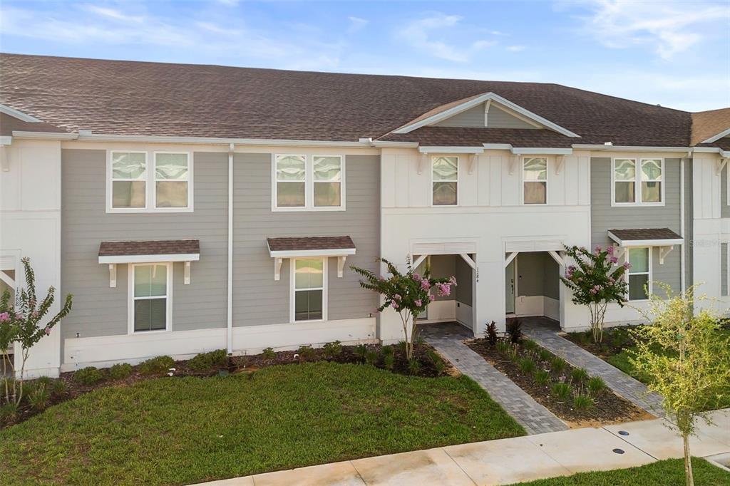 A two-story townhouse exterior with gray and white siding, a shingled roof, and landscaped walkways — 1284 BLUE ISLAND DRIVE, CLERMONT, FL