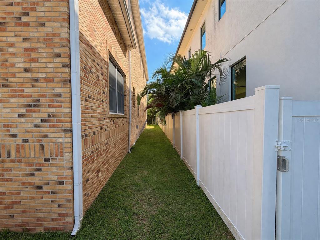 A narrow grassy side yard sits between a brick house and a white vinyl fence — 441 LUCERNE AVENUE, TAMPA, FL