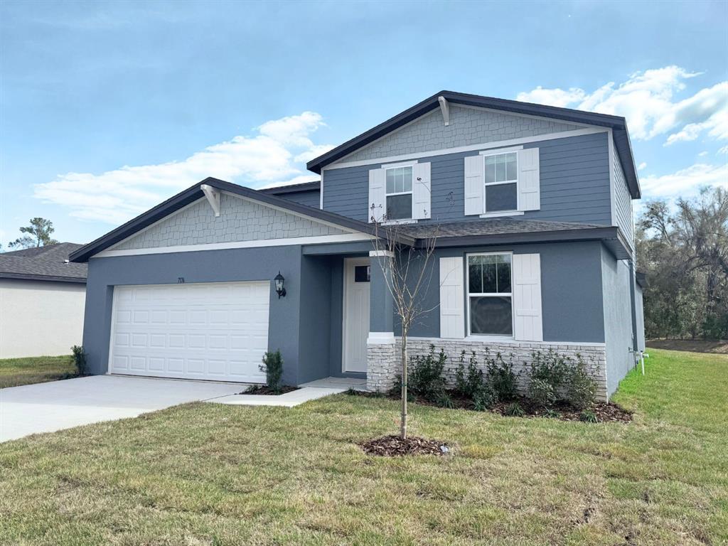 A two-story house with blue siding, a white garage door, and a stone-accented front entrance — 7176 RAY CREEK DRIVE, BROOKSVILLE, FL