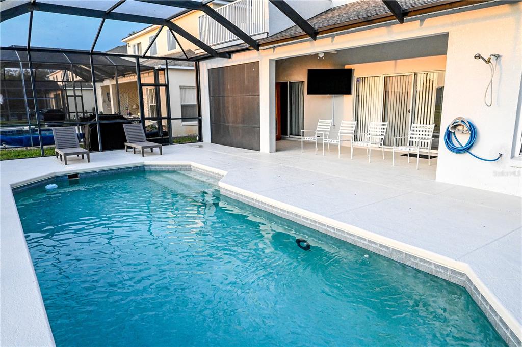 A screened-in pool patio features a rectangular swimming pool, white chairs, and a wall-mounted television — 4733 CUMBRIAM LAKES DRIVE, KISSIMMEE, FL