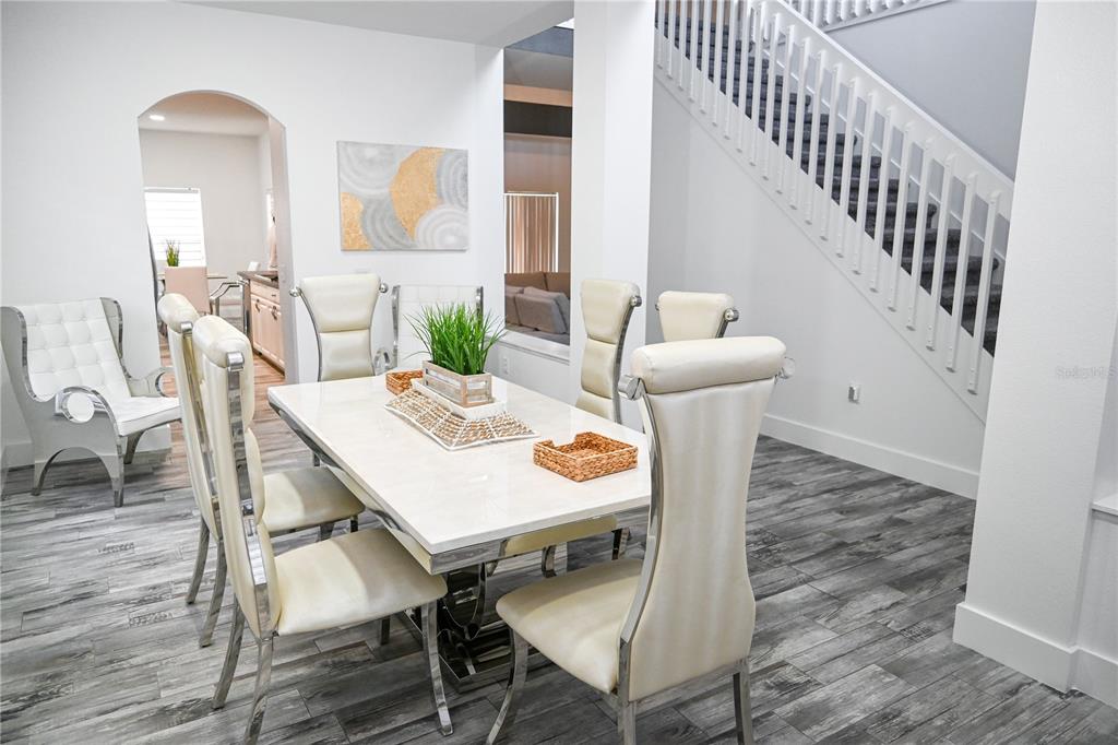 A dining room features a white table, cream chairs, wood-look flooring, and a staircase — 4733 CUMBRIAM LAKES DRIVE, KISSIMMEE, FL