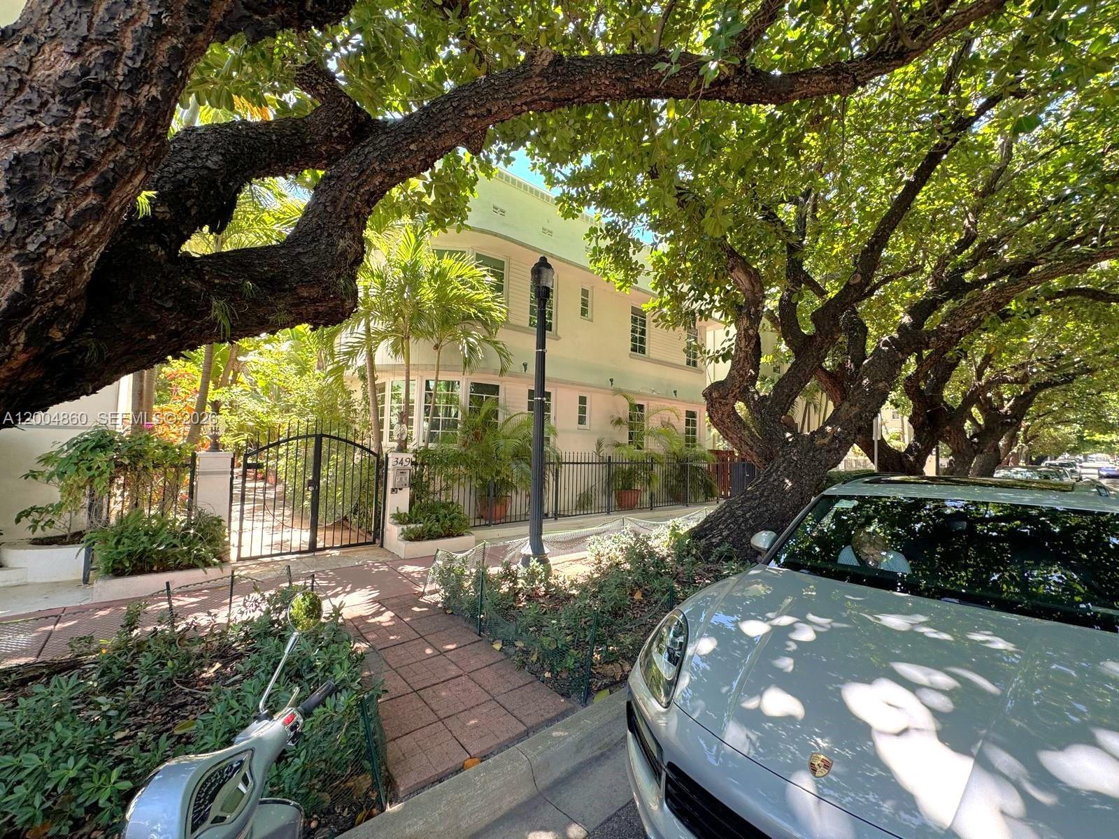 A light-colored two-story building with curved windows is partially obscured by large, leafy trees — 349 Meridian Ave # B202, Miami Beach FL 33139, MIAMI BEACH, FL