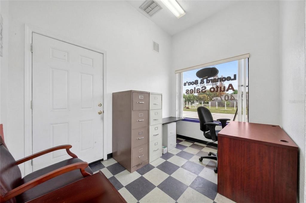 An office space features a checkered floor, a desk, filing cabinets, and a window view — 595 9TH STREET UNIT 115, WINTER GARDEN, FL