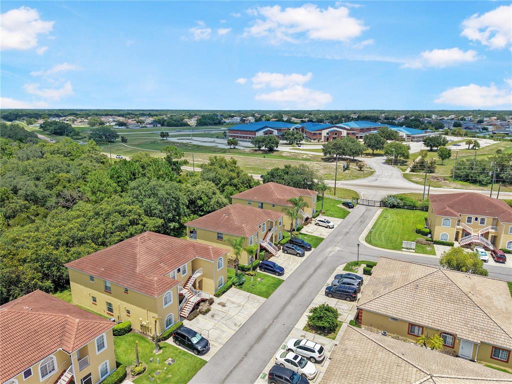 An aerial view shows multi-story apartment buildings with parking spaces and a nearby school complex — 12201 INDIAN CREEK DRIVE, POINCIANA, FL