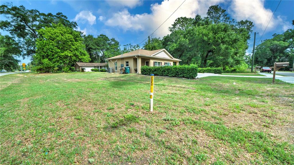 A tan house sits on a large grassy lot surrounded by trees under a blue sky — 1404 NW 18TH AVENUE, OCALA, FL