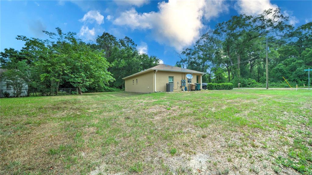 A tan house sits on a large, grassy lot surrounded by trees under a blue sky — 1404 NW 18TH AVENUE, OCALA, FL