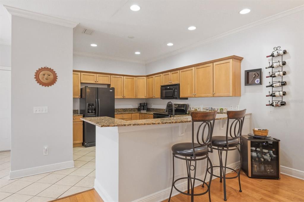 A kitchen with light wood cabinets, granite countertops, a black refrigerator, and a breakfast bar — 208 VALENCIA CIRCLE, ST PETERSBURG, FL