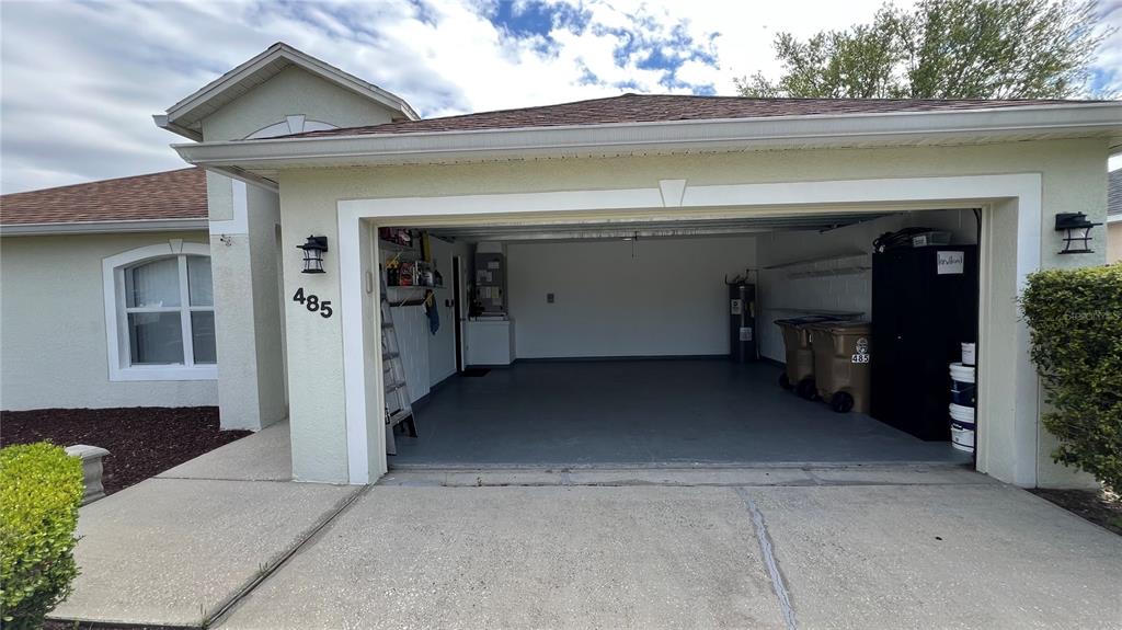 An open garage with a concrete floor, storage shelves, and a water heater — 485 MARTIGUES DRIVE, KISSIMMEE, FL