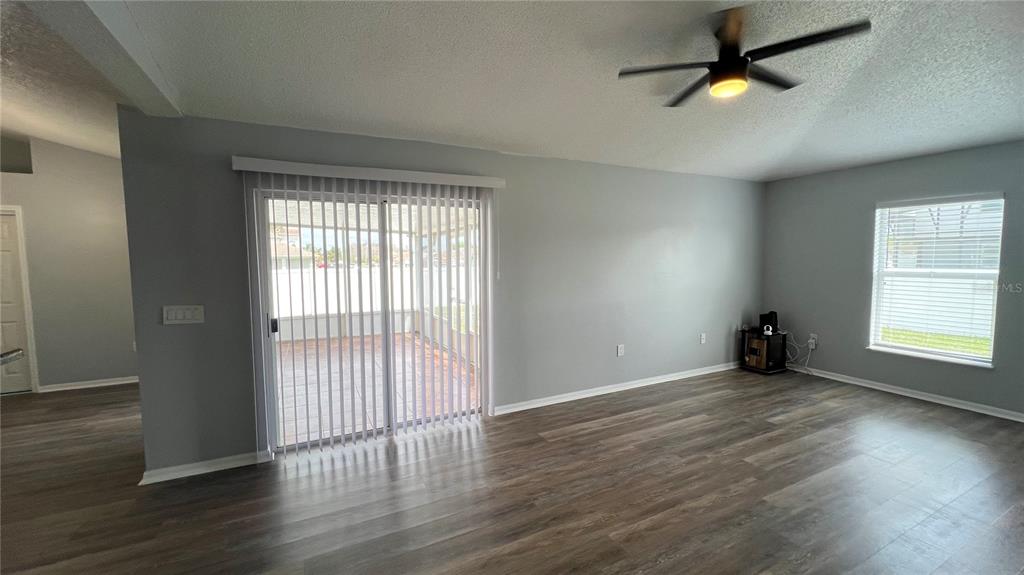 A living room features gray walls, wood-look flooring, a ceiling fan, and sliding glass doors — 485 MARTIGUES DRIVE, KISSIMMEE, FL