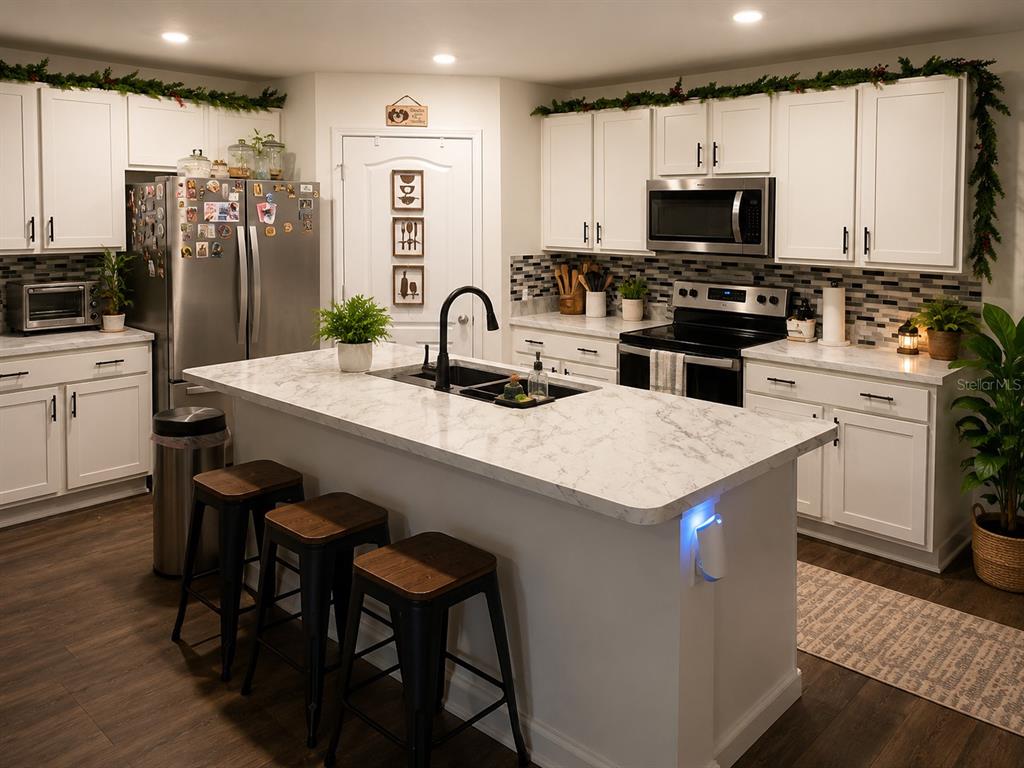 A kitchen features white cabinets, a marble-topped island with bar stools, and stainless steel appliances — 5418 HOLLOW BIRCH DRIVE, JACKSONVILLE, FL