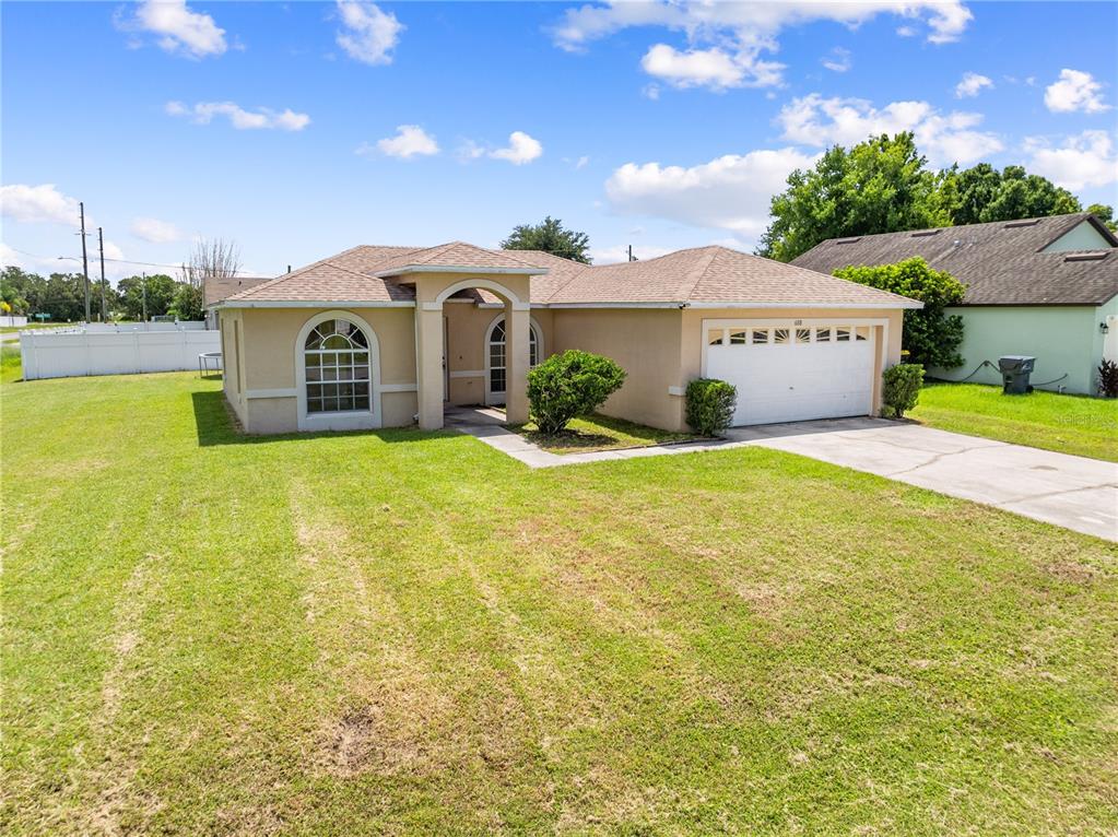 A single-story tan house with a two-car garage and a large front lawn — 688 JAGUAR COURT, POINCIANA, FL
