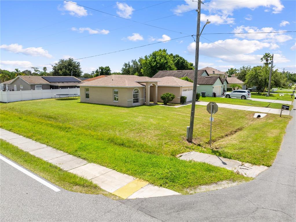 A tan single-story house with a hip roof sits on a corner lot with grass — 688 JAGUAR COURT, POINCIANA, FL