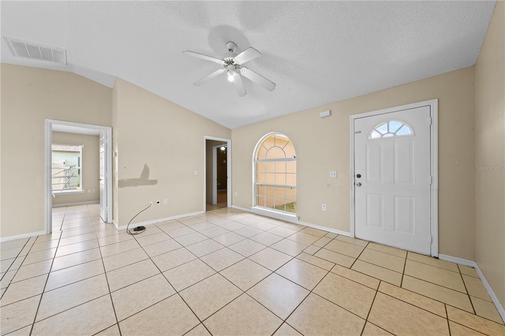 An empty room with beige walls, tile flooring, a ceiling fan, and an arched window — 688 JAGUAR COURT, POINCIANA, FL
