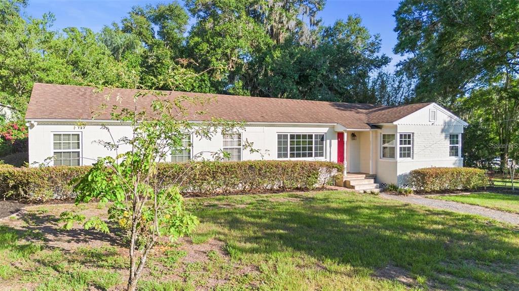 A single-story white brick house with a brown roof and a bright red front door — 611 N GARFIELD AVENUE, DELAND, FL