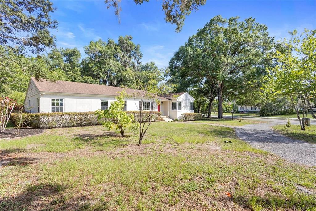A white, single-story house with a gravel driveway sits on a grassy lot with trees — 611 N GARFIELD AVENUE, DELAND, FL