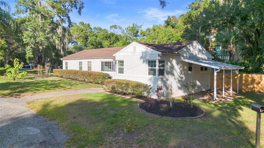 A single-story house with a light-colored brick exterior, a gravel driveway, and a side carport — 611 N GARFIELD AVENUE, DELAND, FL