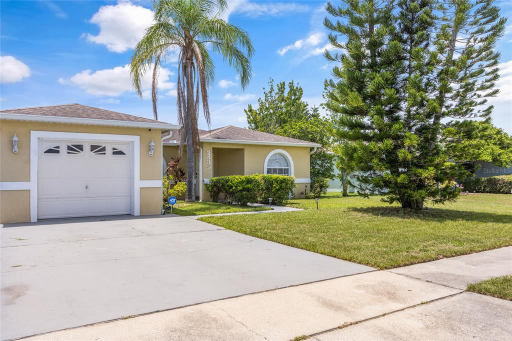 A single-story house with a garage, a palm tree, and a large evergreen tree — 2430 QUAIL RUN BOULEVARD, KISSIMMEE, FL