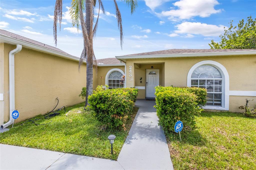 A single-story house exterior features a beige stucco facade, arched windows, and a front walkway — 2430 QUAIL RUN BOULEVARD, KISSIMMEE, FL