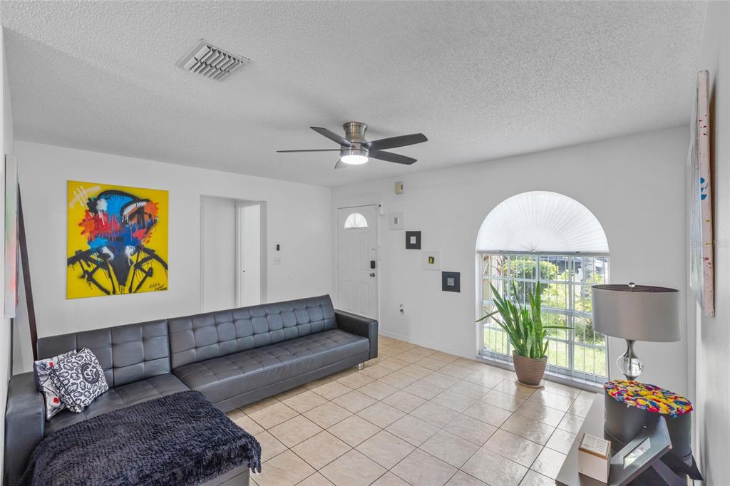 A living room features a black sectional sofa, tiled floors, a ceiling fan, and arched window — 2430 QUAIL RUN BOULEVARD, KISSIMMEE, FL