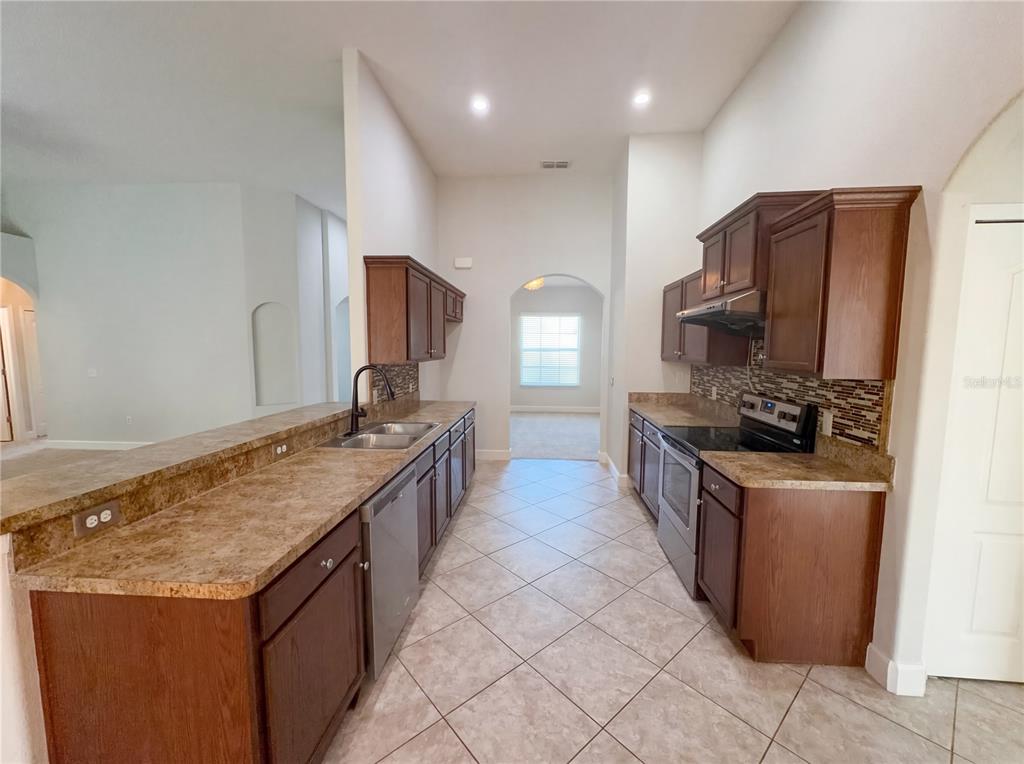 A kitchen features dark wood cabinets, laminate countertops, stainless steel appliances, and tile flooring — 6326 HICKORY LEAF PLACE, LAKELAND, FL