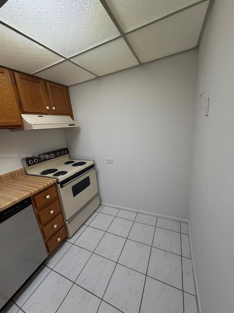 A kitchen features white tile flooring, wooden cabinets, and a white electric stove — 3720 Inverrary Dr # 2K, Lauderhill FL 33319, LAUDERHILL, FL