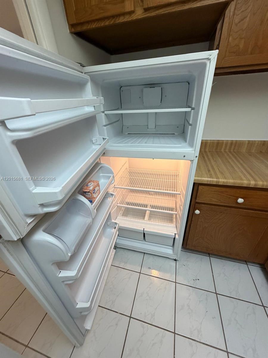 A white top-freezer refrigerator stands in a kitchen with wood cabinets and tiled floors — 3720 Inverrary Dr # 2K, Lauderhill FL 33319, LAUDERHILL, FL