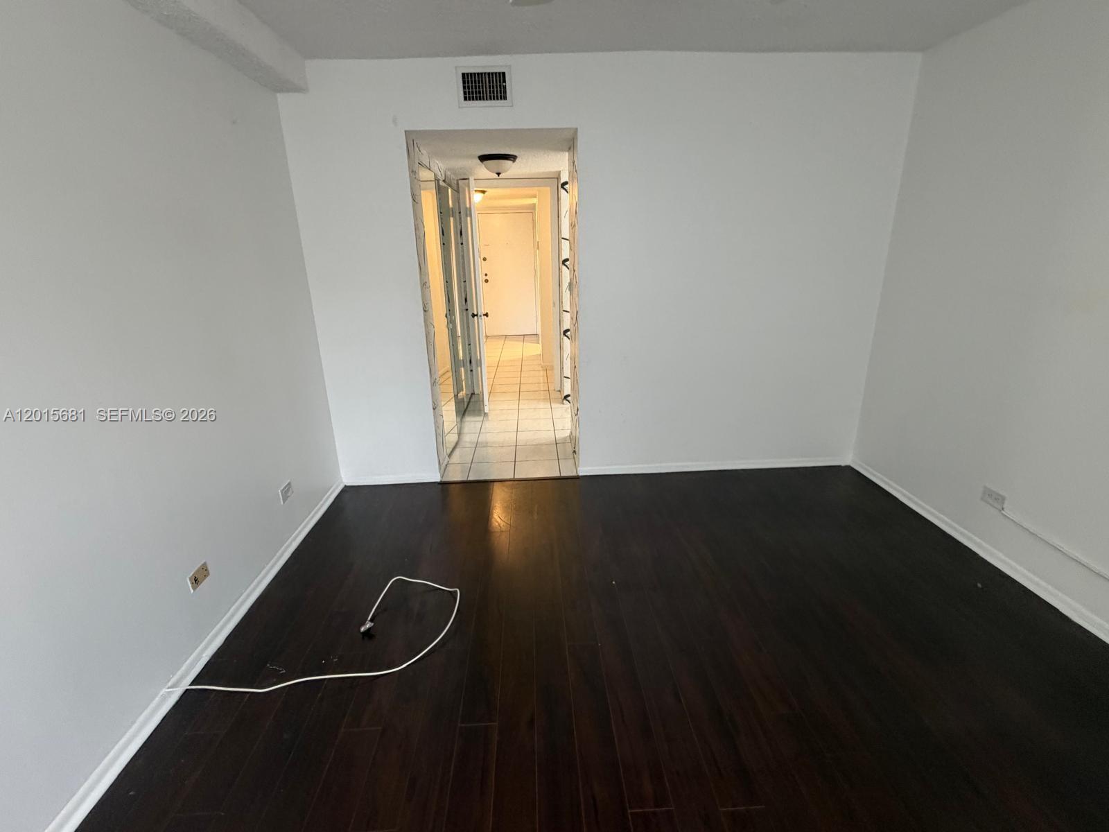 A room with dark wood flooring and white walls leads to a tiled hallway — 3720 Inverrary Dr # 2K, Lauderhill FL 33319, LAUDERHILL, FL