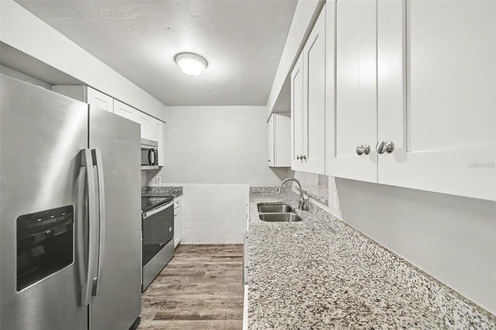 A galley kitchen features white cabinets, granite countertops, stainless steel appliances, and wood-look flooring — 4814 BLARNEY DRIVE, ORLANDO, FL