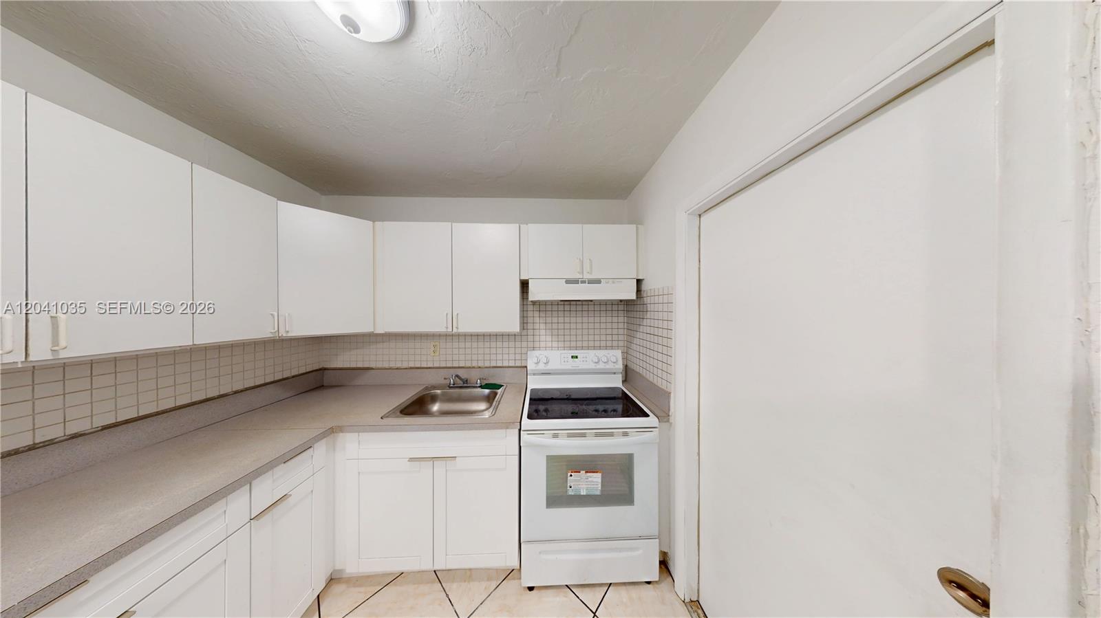 A small kitchen features white cabinets, a white stove, and a stainless steel sink — 6811 SW 16th St, Miami FL 33155, MIAMI, FL
