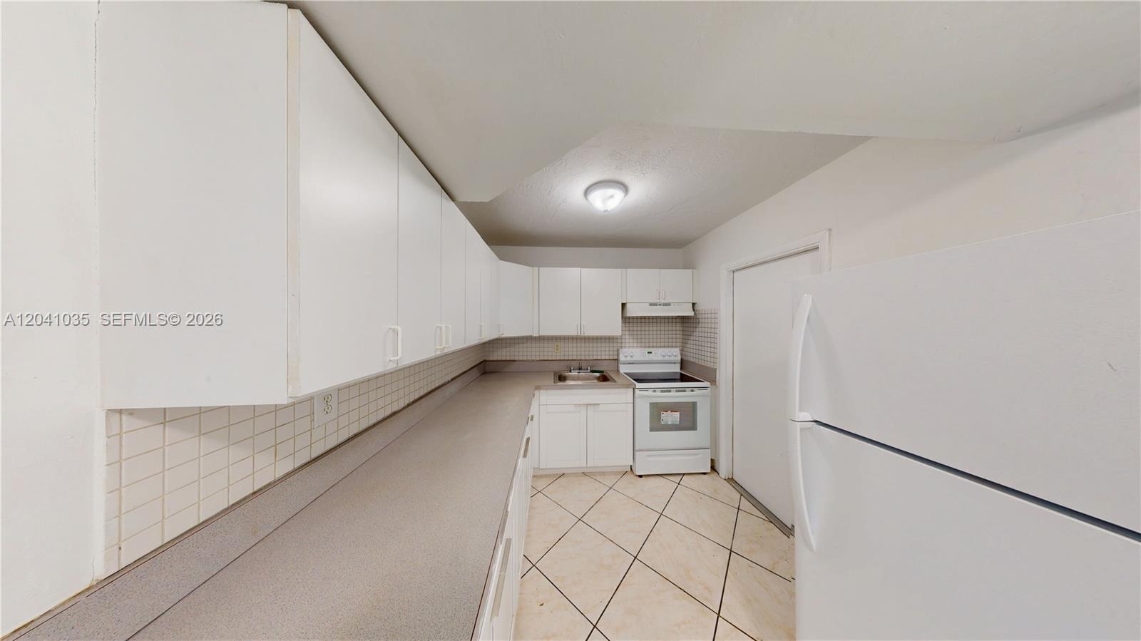 A kitchen features white cabinets, a gray countertop, a white stove, and tiled flooring — 6811 SW 16th St, Miami FL 33155, MIAMI, FL