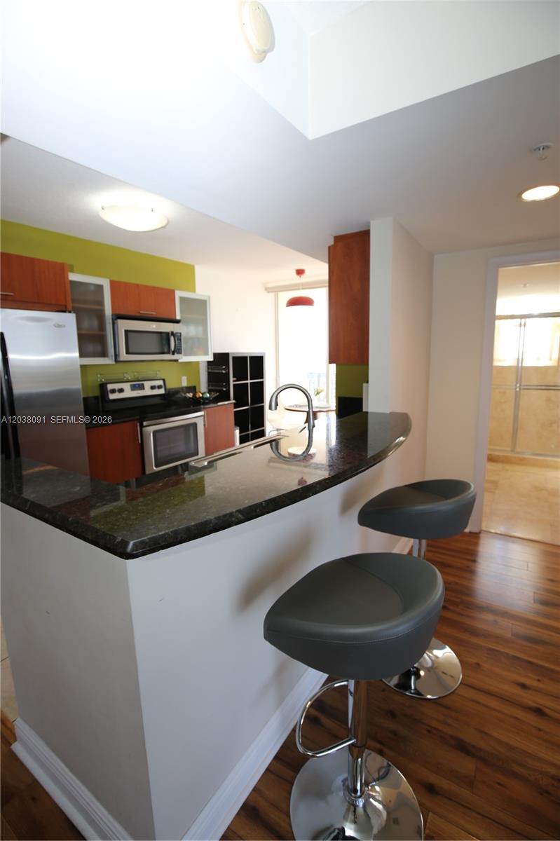 A kitchen features a curved granite breakfast bar with two gray stools and wood flooring — 3232 SW 22nd Ter # 1510, Miami FL 33145, MIAMI, FL