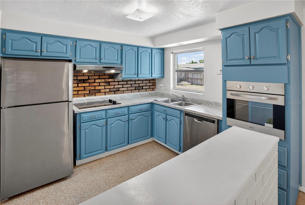 A kitchen features blue cabinets, stainless steel appliances, a brick backsplash, and white countertops — 13746 MARTINIQUE DRIVE, SEMINOLE, FL