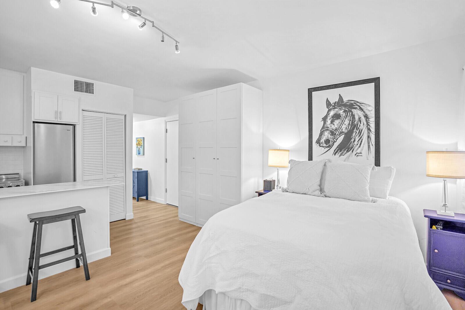 A studio apartment features a kitchen, a bed, a large wardrobe, and light wood flooring — 11863 Wimbledon Circle # 423, Wellington FL 33414, WELLINGTON, FL