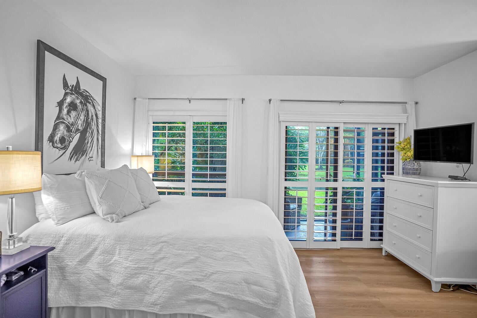 A bedroom with white bedding, a horse print, plantation shutters, and a white dresser — 11863 Wimbledon Circle # 423, Wellington FL 33414, WELLINGTON, FL