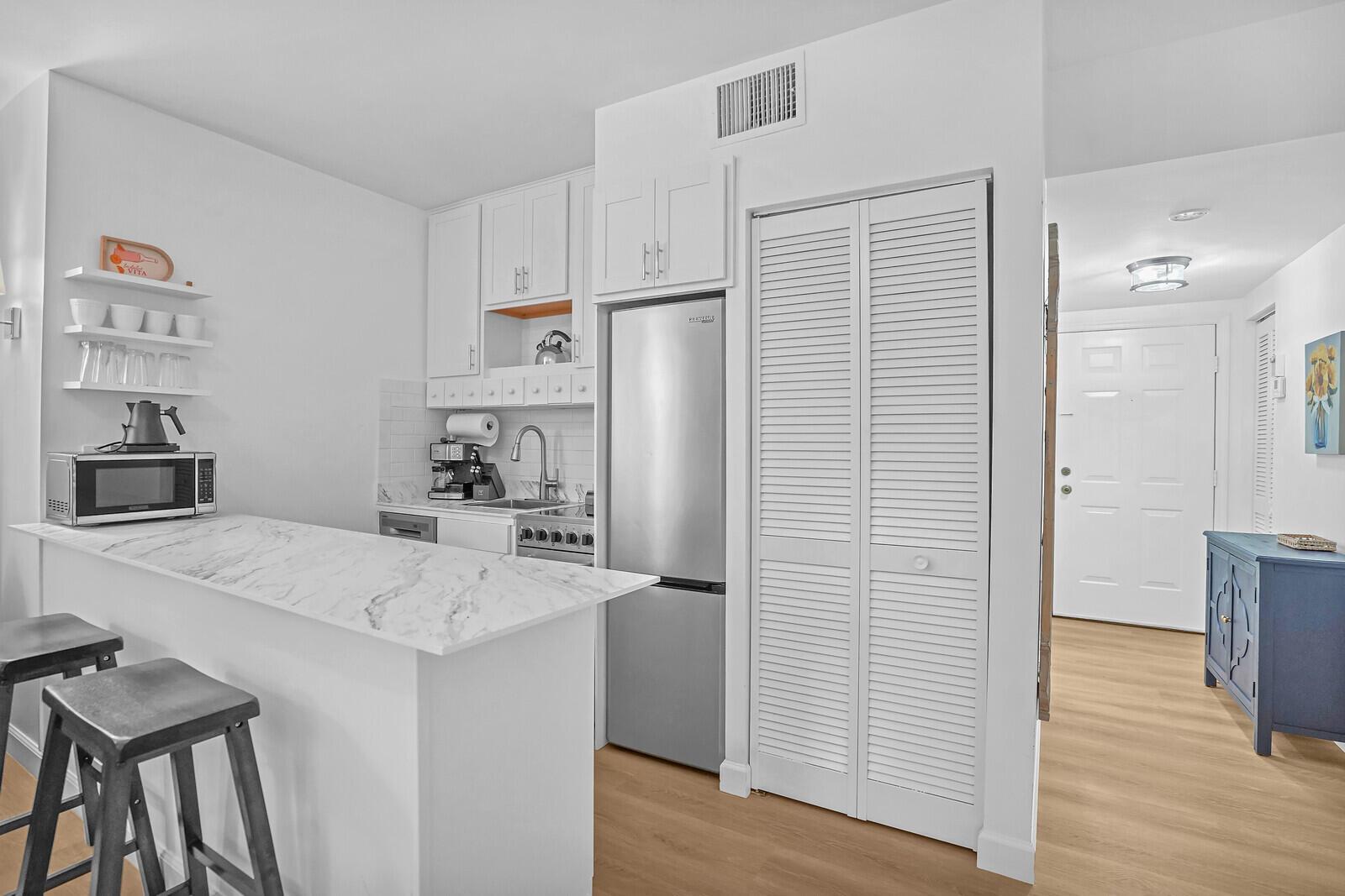 A small kitchen features white cabinets, a marble-topped breakfast bar, and stainless steel appliances — 11863 Wimbledon Circle # 423, Wellington FL 33414, WELLINGTON, FL