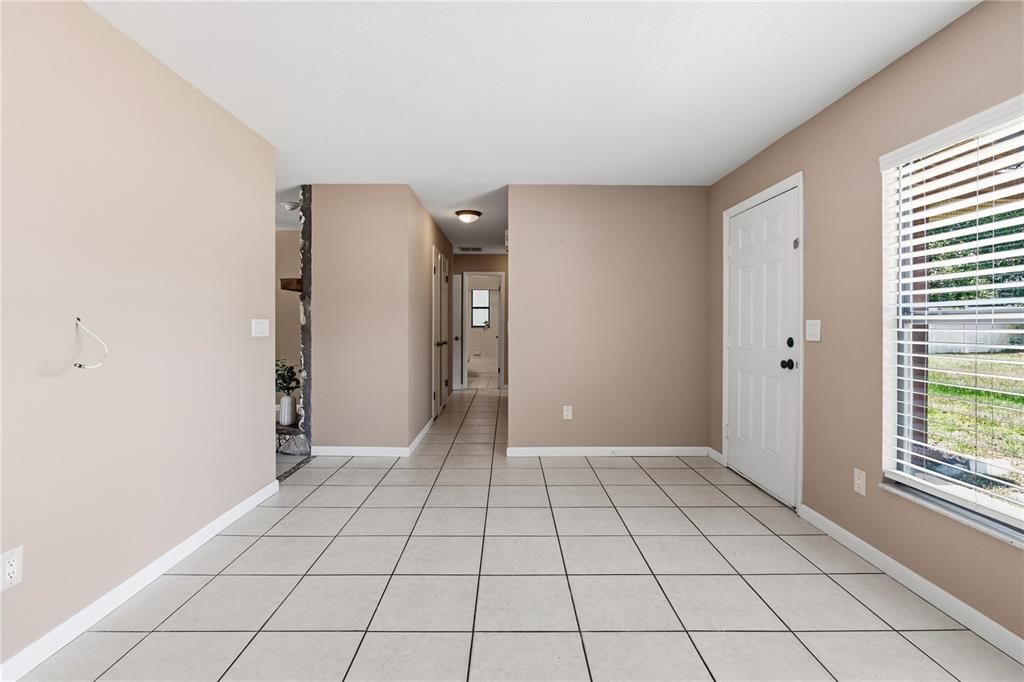 A room with beige walls, white tile flooring, a front door, and a hallway entrance — 214 E FLOYD AVENUE, LAKE MARY, FL