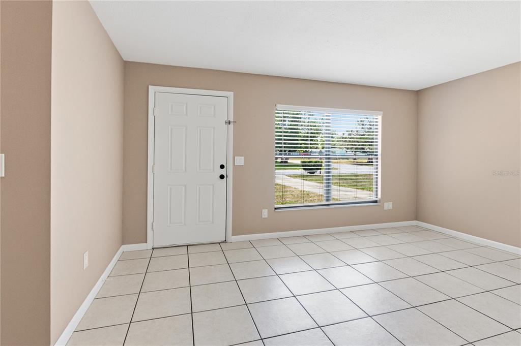 An empty room features beige walls, white trim, and light-colored square floor tiles — 214 E FLOYD AVENUE, LAKE MARY, FL