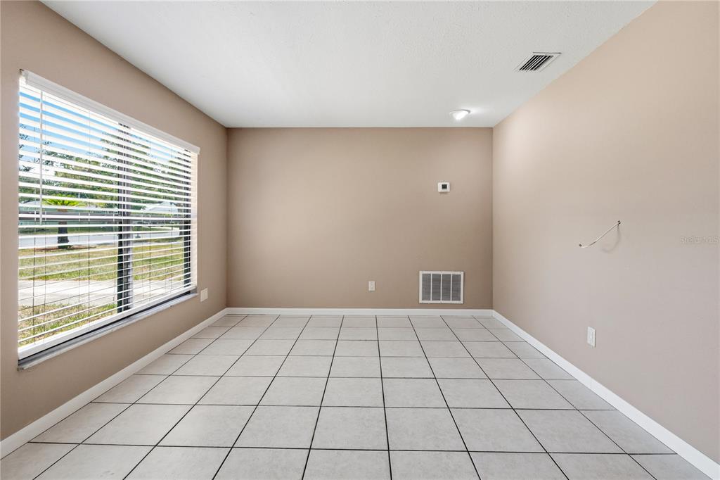 An empty room with beige walls, white tile flooring, and a large window with blinds — 214 E FLOYD AVENUE, LAKE MARY, FL