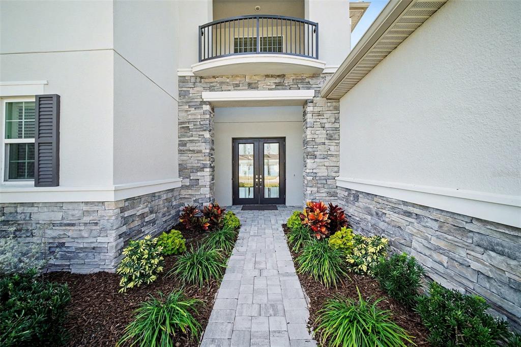 A stone-accented entryway features a paved walkway leading to double front doors and a balcony — 3263 JUNIPER SPRINGS STREET, WESLEY CHAPEL, FL
