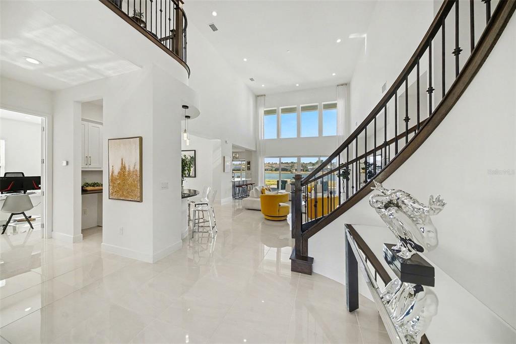 A bright, high-ceilinged foyer features a curved staircase, tile flooring, and a view of water — 3263 JUNIPER SPRINGS STREET, WESLEY CHAPEL, FL