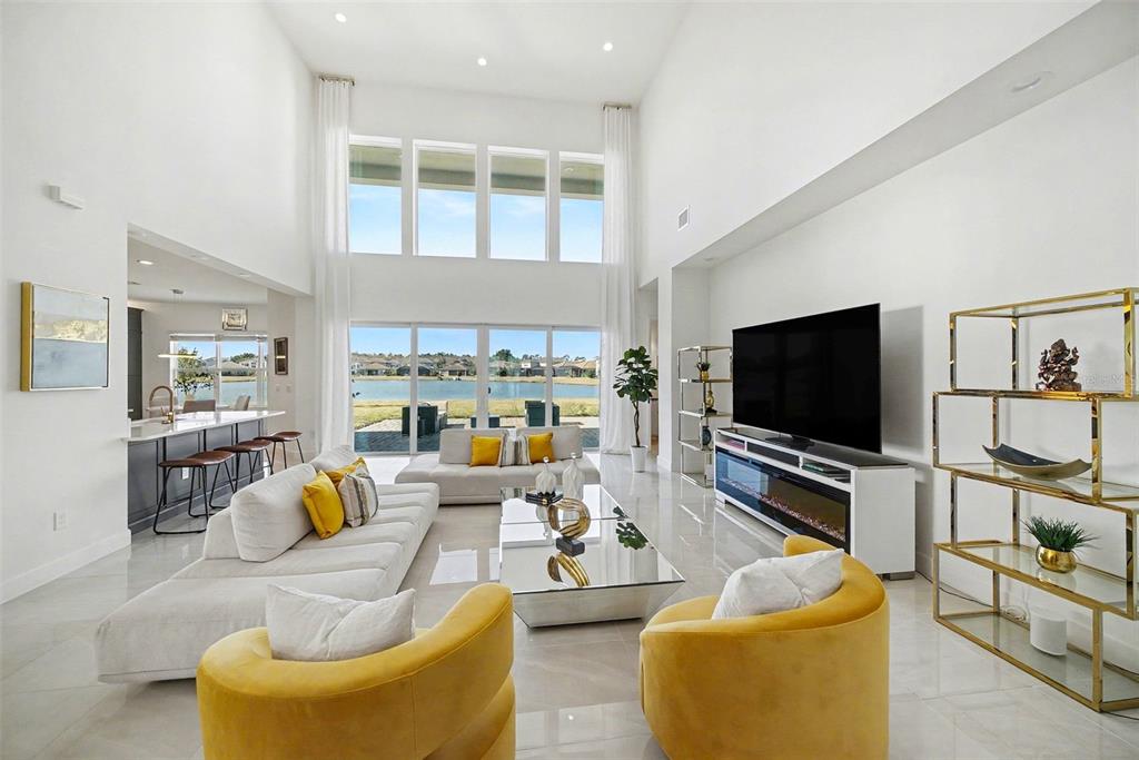 A bright, high-ceilinged living room features white furniture, yellow accent chairs, and a lake view — 3263 JUNIPER SPRINGS STREET, WESLEY CHAPEL, FL