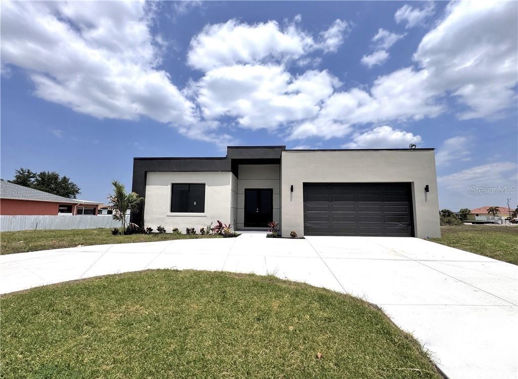 A modern, single-story house features a flat roof, stucco exterior, and a two-car garage — 1247 KISMET PARKWAY W, CAPE CORAL, FL