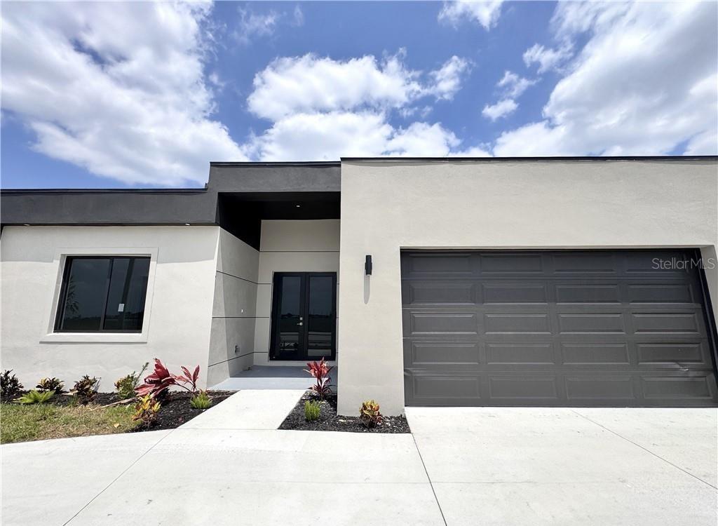 A modern single-story house features a white stucco exterior, dark trim, and a double-car garage — 1247 KISMET PARKWAY W, CAPE CORAL, FL