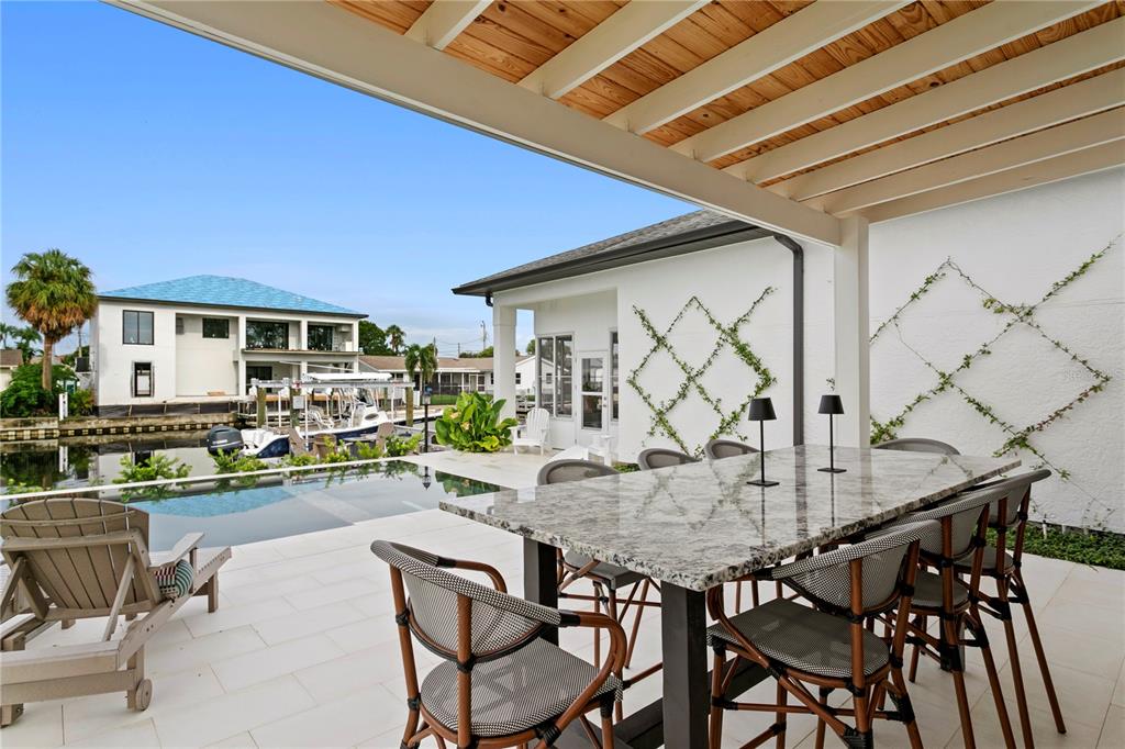 A covered outdoor patio features a granite dining table, chairs, and a pool overlooking a canal — 4091 13TH WAY NE, ST PETERSBURG, FL
