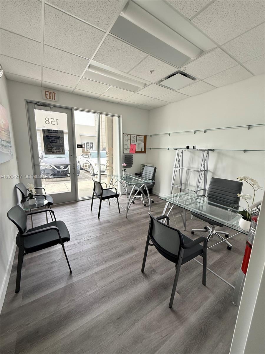 An office space features glass desks, black chairs, wood-look flooring, and a glass entry door — SWEETWATER, FL