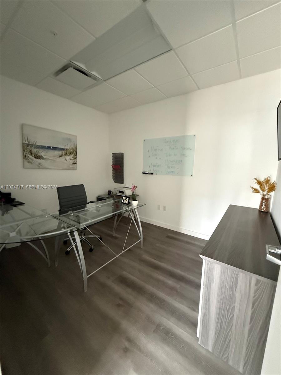 An office features a glass desk, a whiteboard, and wood-look flooring — SWEETWATER, FL