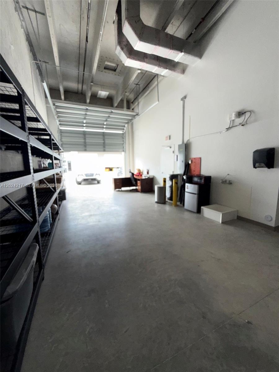 This industrial warehouse space features high ceilings, exposed ductwork, concrete floors, and metal shelving — SWEETWATER, FL